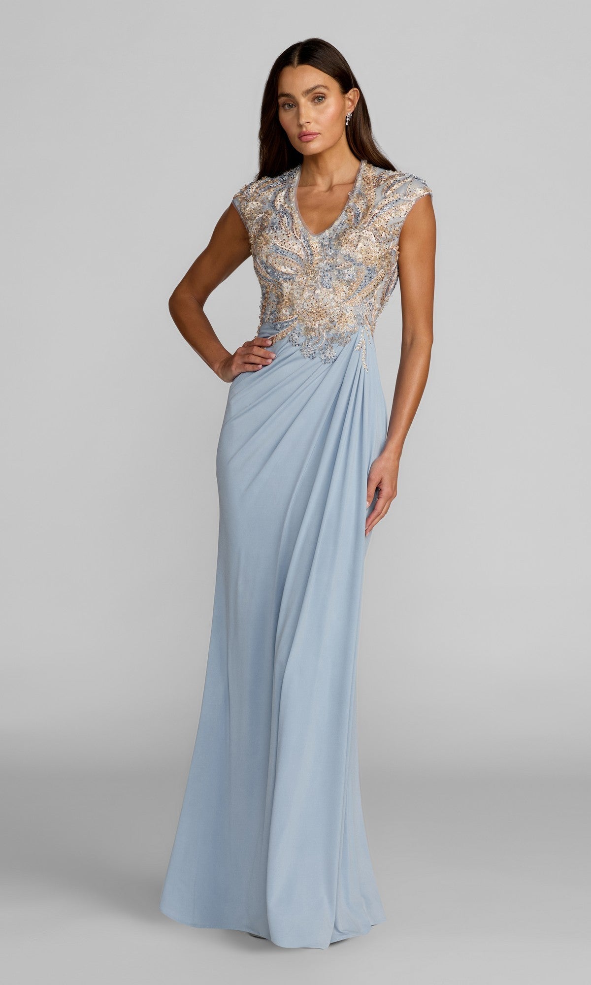 A woman stands against a plain grey background wearing the Mac Duggal 21330 long formal dress in French Blue—a floor-length evening gown crafted from jersey, featuring a beaded and embroidered bodice with cap sleeves and a delicate v-neckline.